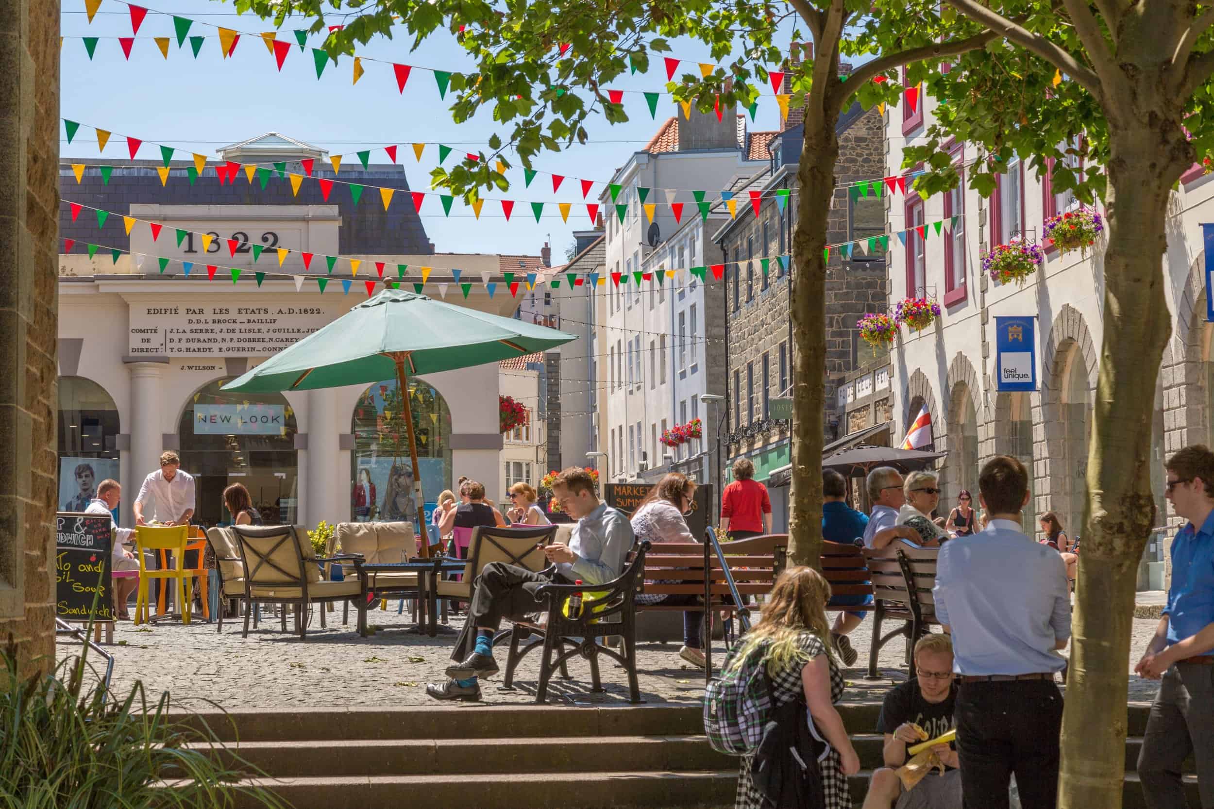 Vibrant outdoor scene at Guernsey ferry terminal with visitors enjoying sunny weather and colourful.