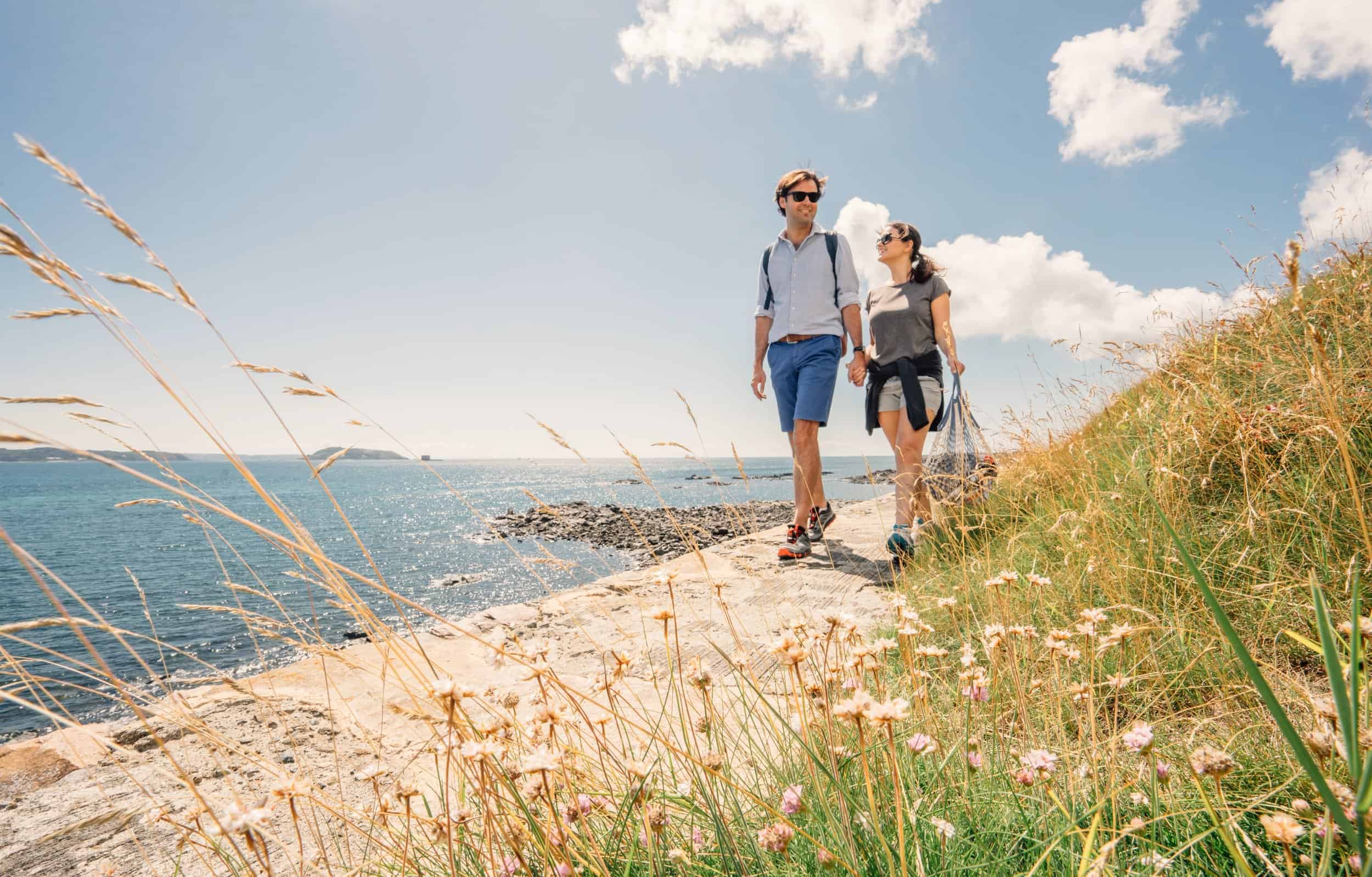 Couple walking along the coast of Guernsey on a sunny day.
